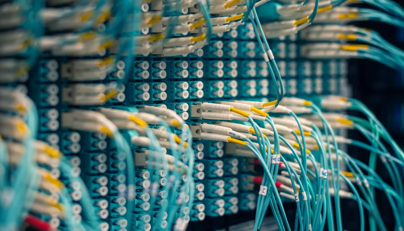 A dense fibre optic patch panel with rows of connectors and bundled aqua patch leads.