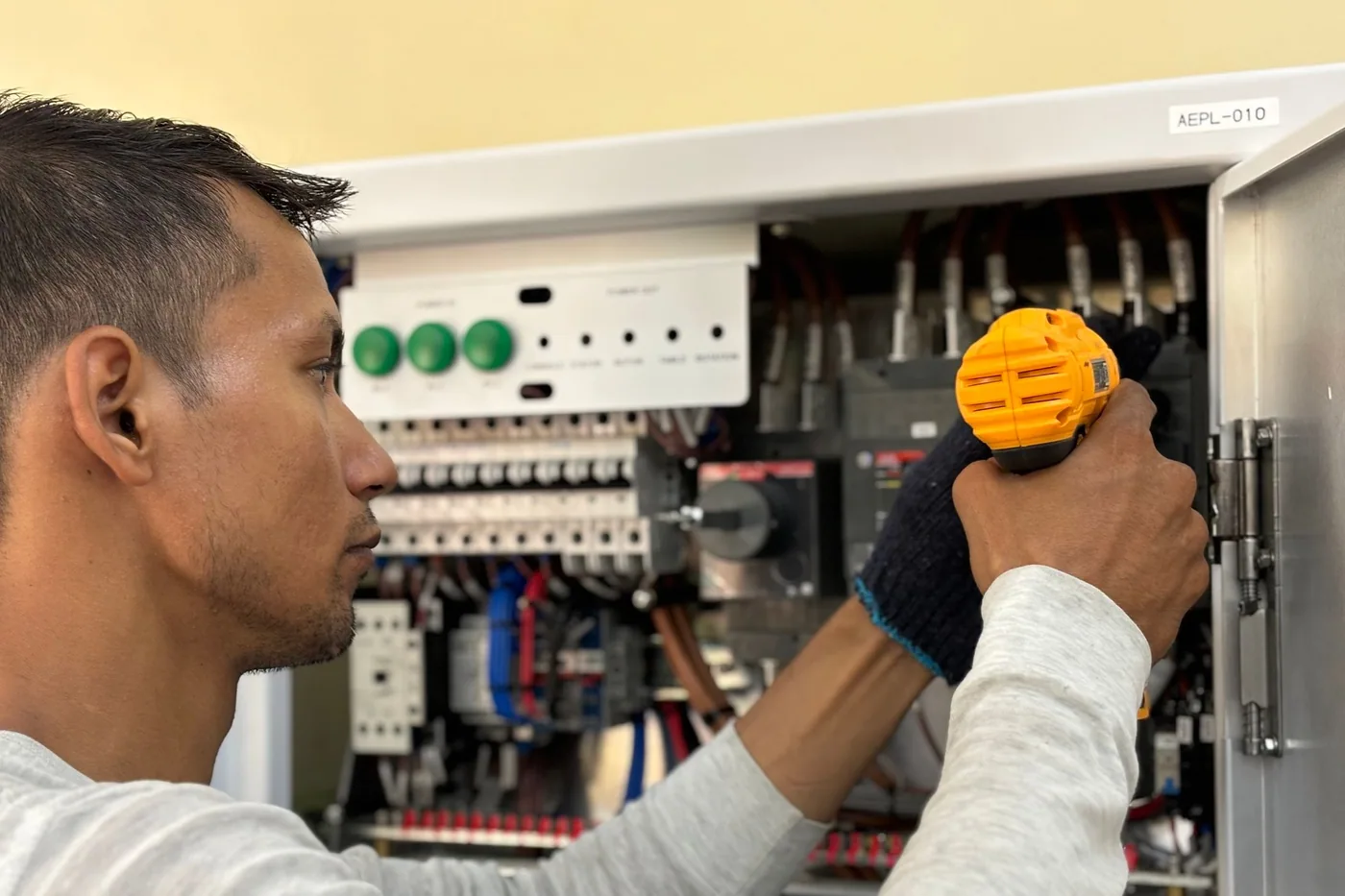 An electrician in protective clothing working on wiring inside an open industrial control cabinet.