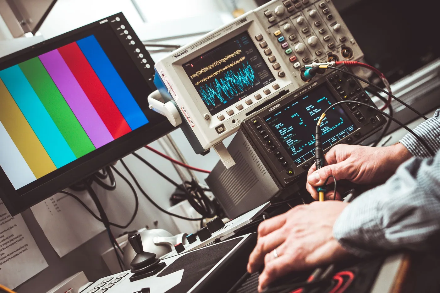 An oscilloscope on a laboratory bench displaying a waveform trace, with probe leads connected to a test board.