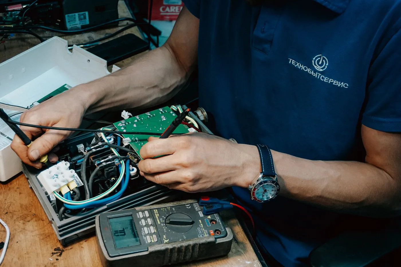 An electrician taking a reading from a wired distribution board using a handheld multimeter.