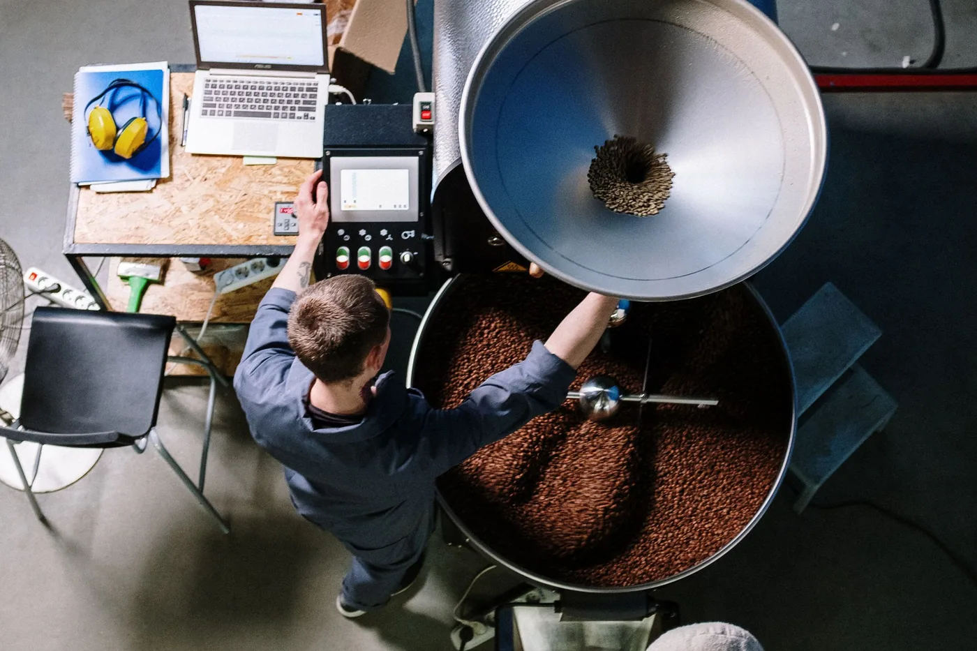 An engineer standing at a production machine with an open laptop, adjusting equipment on the shop floor.