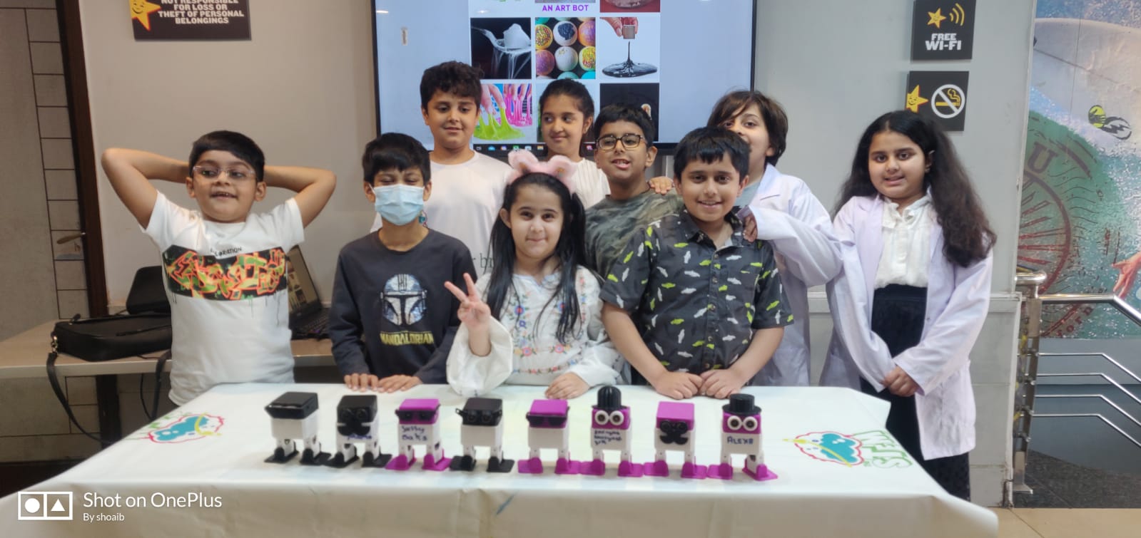 Group of kids smiling next to the row of biped robots they built and named in an Incendio STEM class